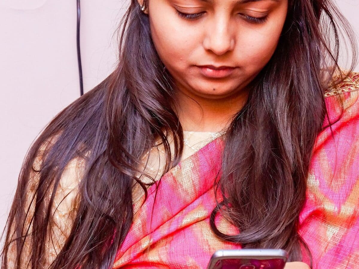 A woman in a festive saree holding her phone privately